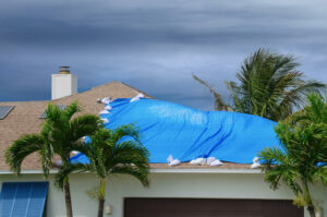 Storm damaged roof of house with protective blue plastic tarp scattered through hole in kettles and on roof.
